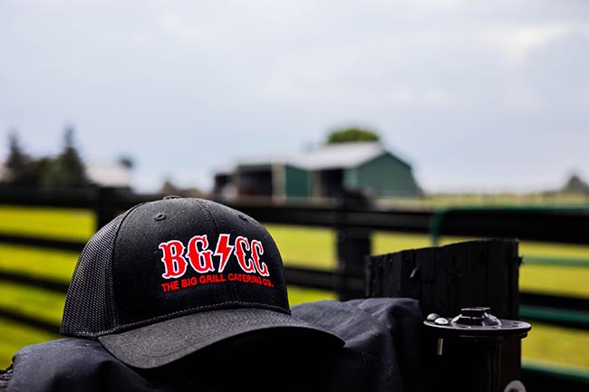 picture of Big Grill Catering hat on a folded uniform with a farm blurred in the background