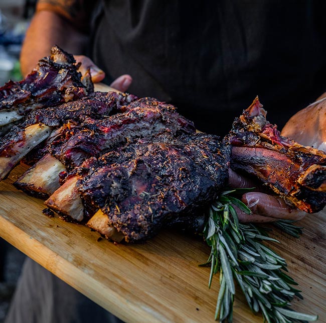 delicious BBQd ribs cut up on a wooden platter with rosemary sprig