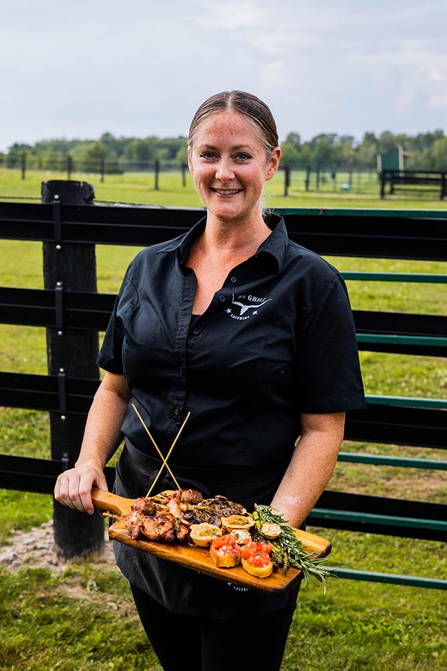 big grill catering server holding a wooden platter with grilled chicken, rosemary sprig for garnish