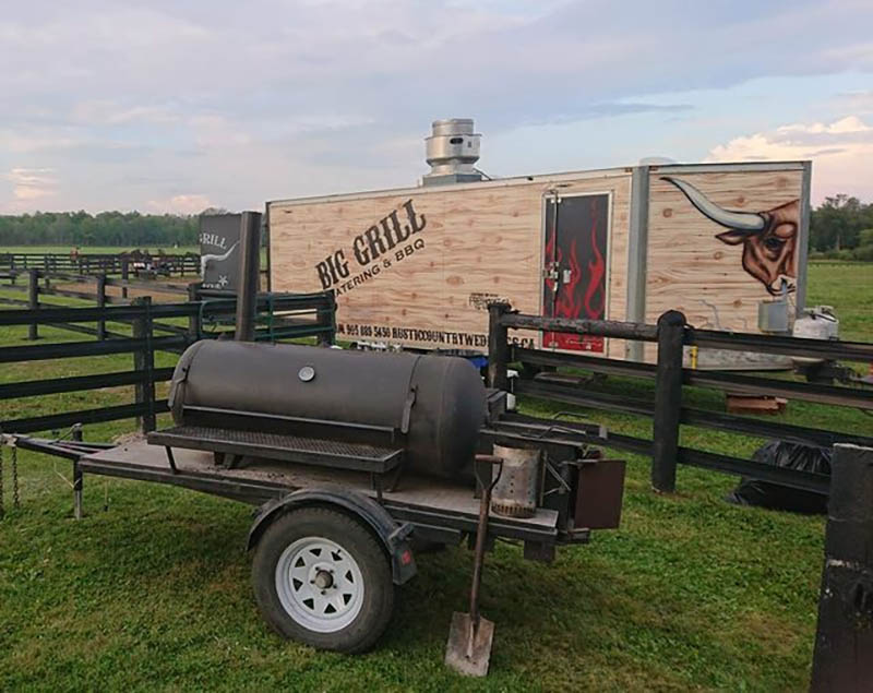 display of Big Grill Caterings trailers, one is a black metal smoker grill and the other is a brown enclosed trailer
