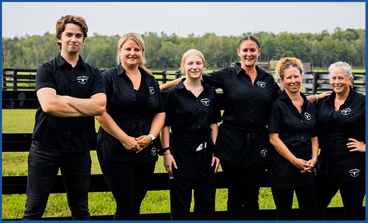 picture of Big Grill Catering Staff dressed in all black, standing in front of a farm fence and fields behind.