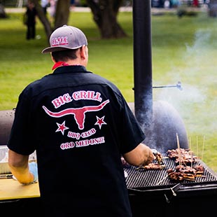 owner Kevin Finch's back grilling on a mobile grill with tall smoke pipe in a park setting